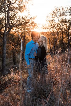 A couple embraces in a romantic sunset moment among tall grass and autumn trees with golden light streaming through.