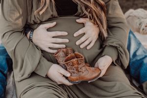 Close-up view of newborn leather baby boots held against a pregnant belly in a cozy setting.
