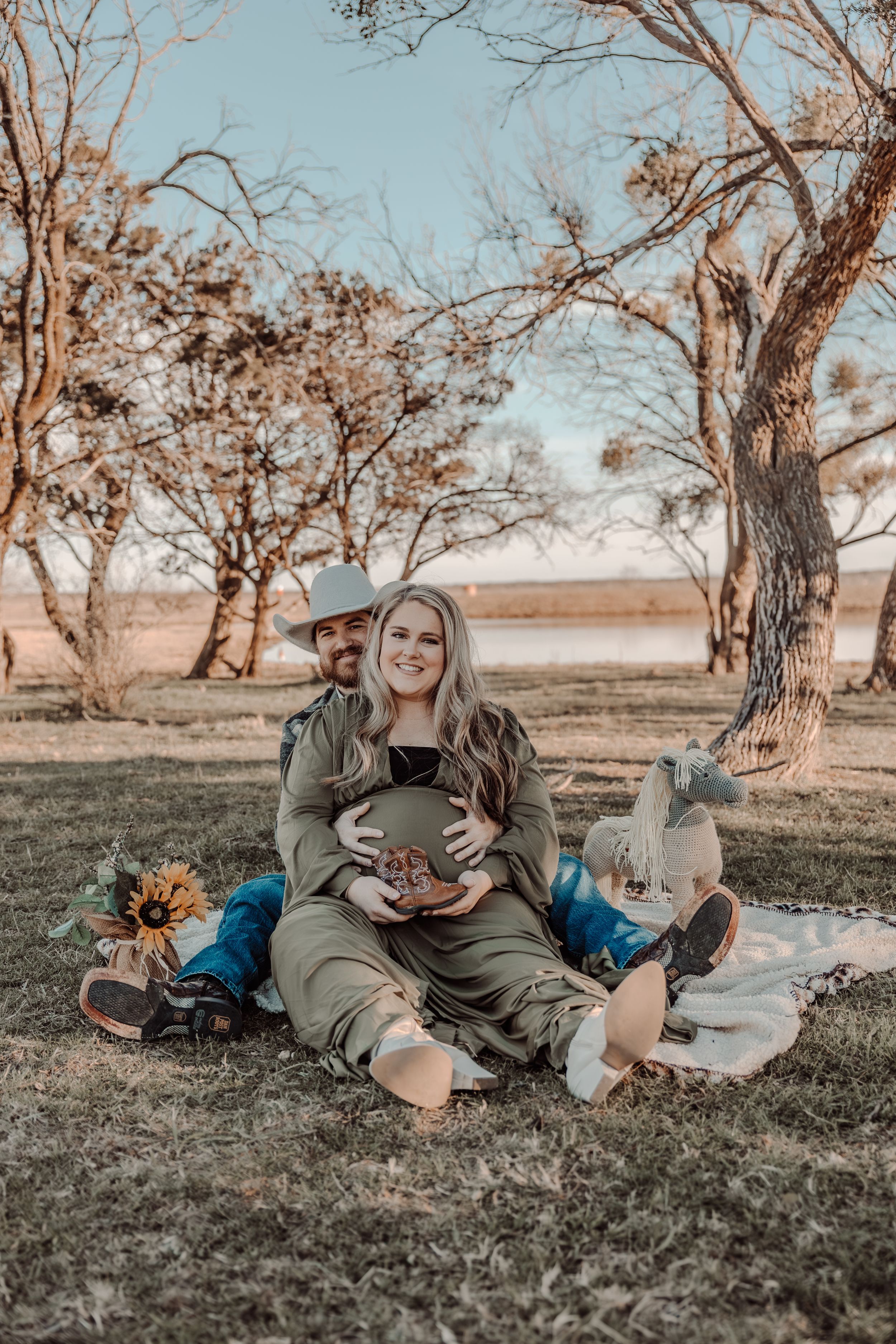 Fall maternity photoshoot outdoors with warm autumn lighting and rustic setting showing person sitting on blanket.