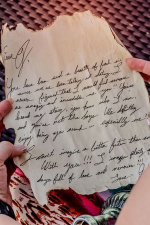 Old handwritten note on aged paper with cursive text held against a textured background pattern.