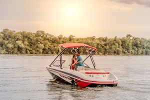 A red and white speedboat cruises on a peaceful river at sunset with trees lining the shoreline.