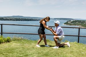 Two people sharing a special moment on a grassy cliff overlooking a scenic coastal bay on a sunny summer day.