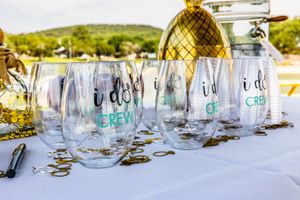 Clear plastic stemless wine glasses with decorative text arranged on white tablecloth with golden pineapple decor in background.