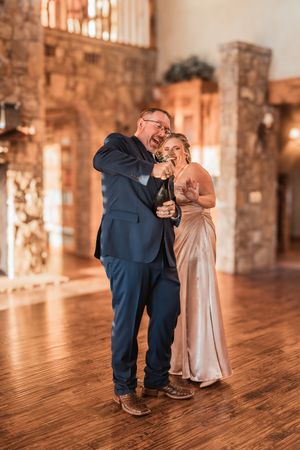 A tender embrace on a wooden dance floor with stone walls and warm lighting in the background.
