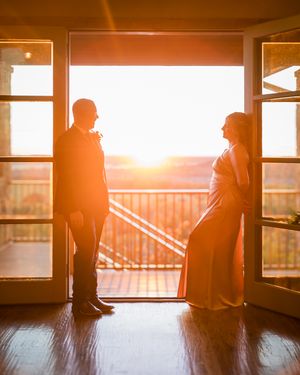 Silhouettes of two people standing in a doorway against a dramatic golden sunset through windows.