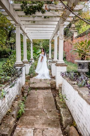 White pergola covered walkway with stone pavers and columns in a lush garden setting creates an elegant outdoor passageway.