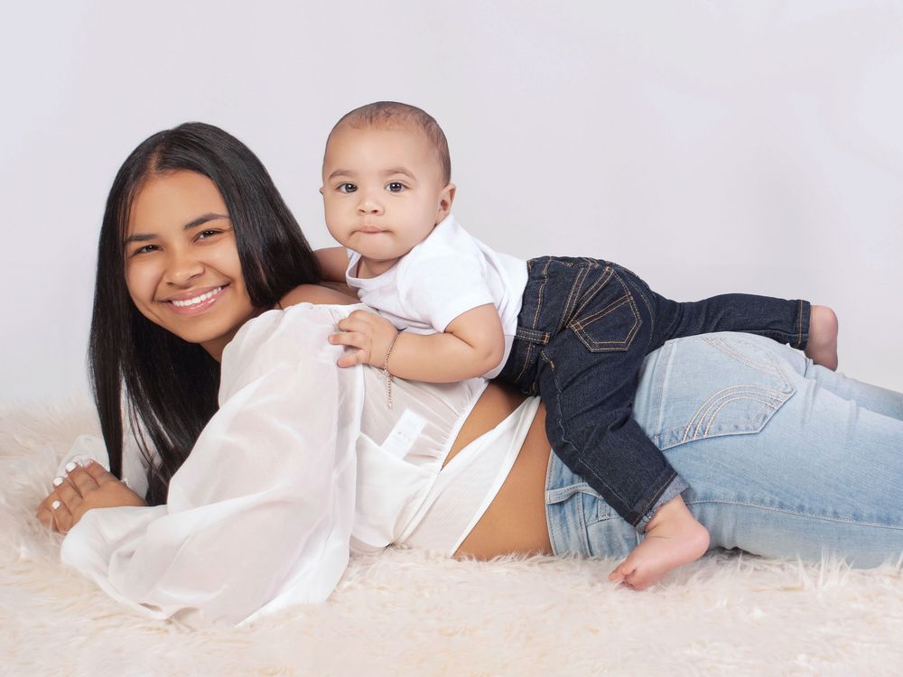 Mother and baby in white and denim outfits resting together on light colored fabric.