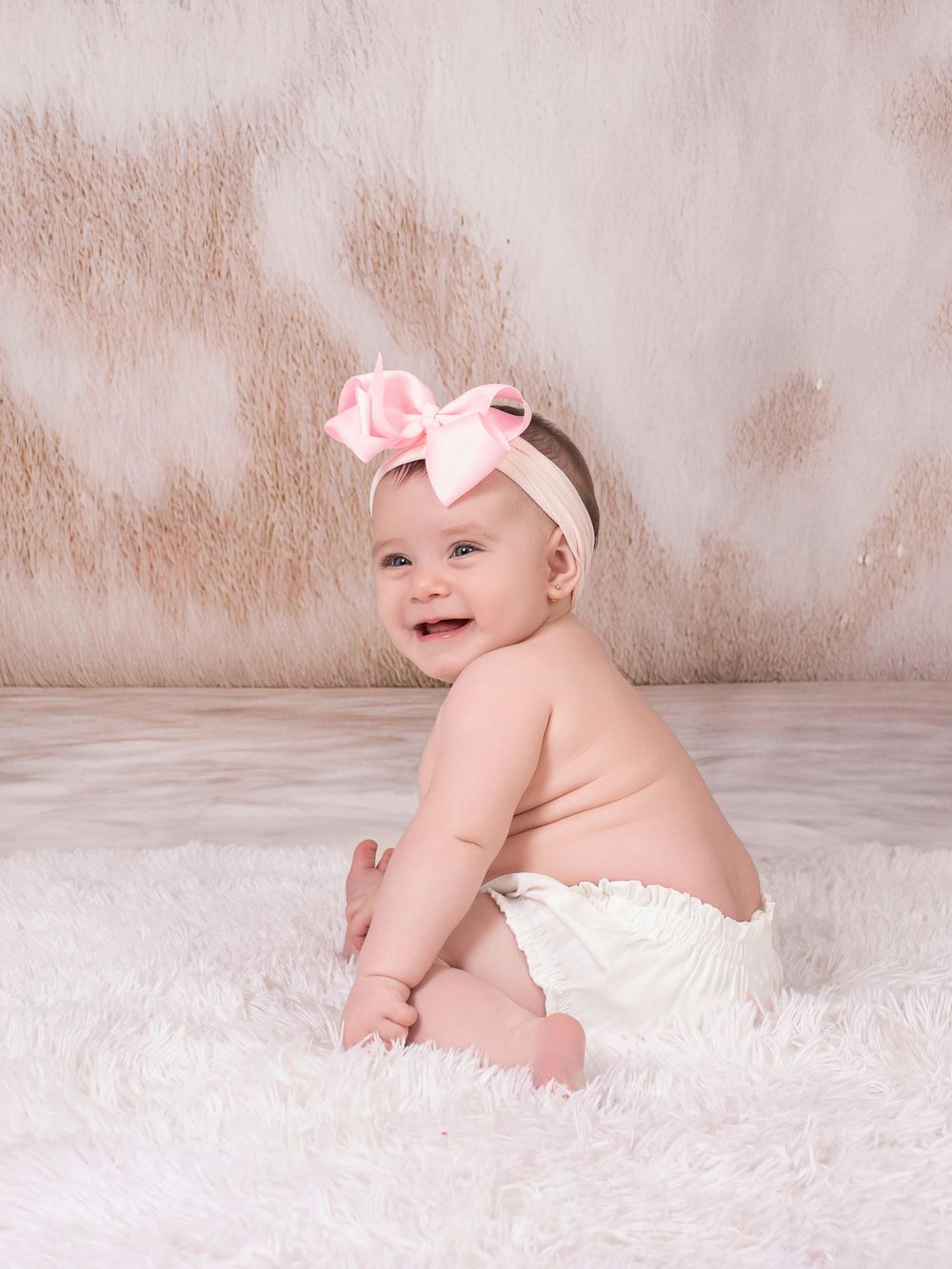 Baby in white diaper poses and plays on soft white rug against neutral beige background in photo series.