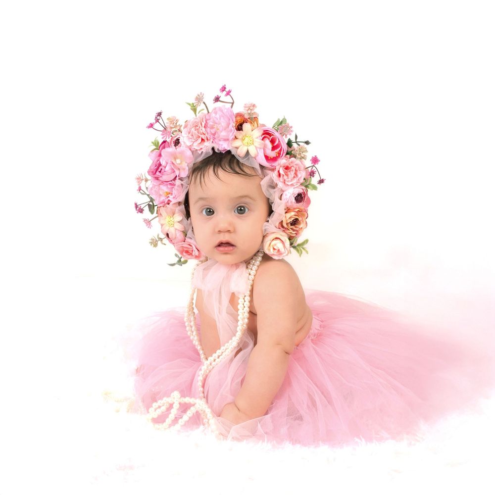 Baby in pink tulle dress wearing floral crown poses for portrait photography session.