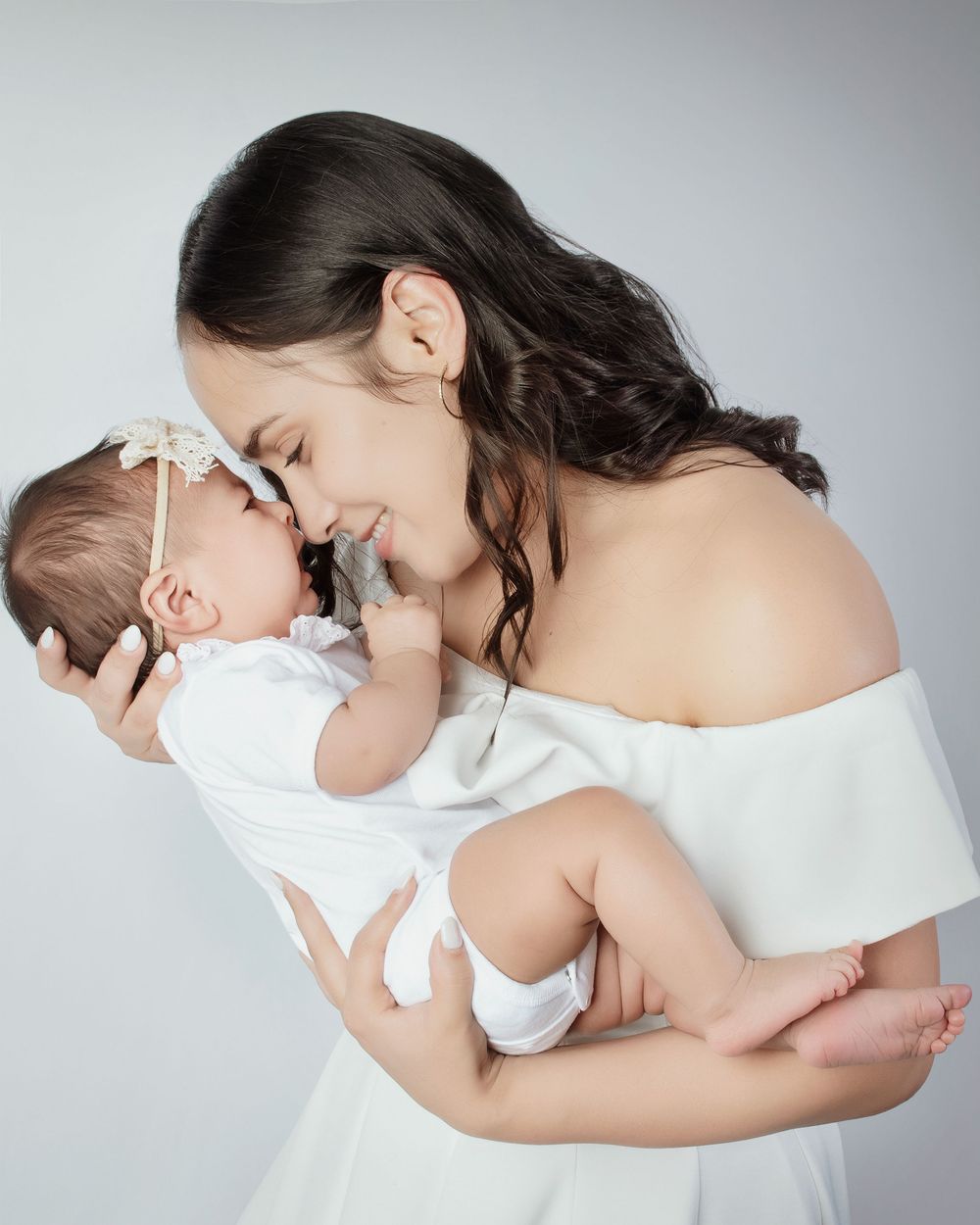A tender embrace between a parent and child wearing white clothing against a light gray background.