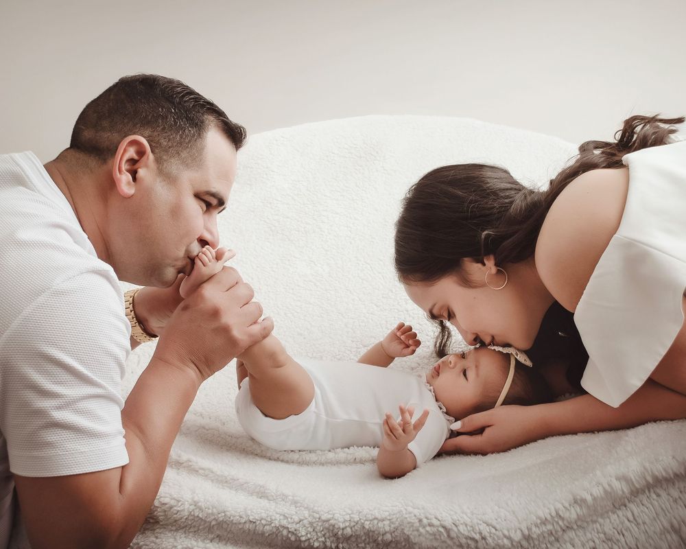 A series of black and white photos showing a parent tenderly bonding with a baby lying on a bed.