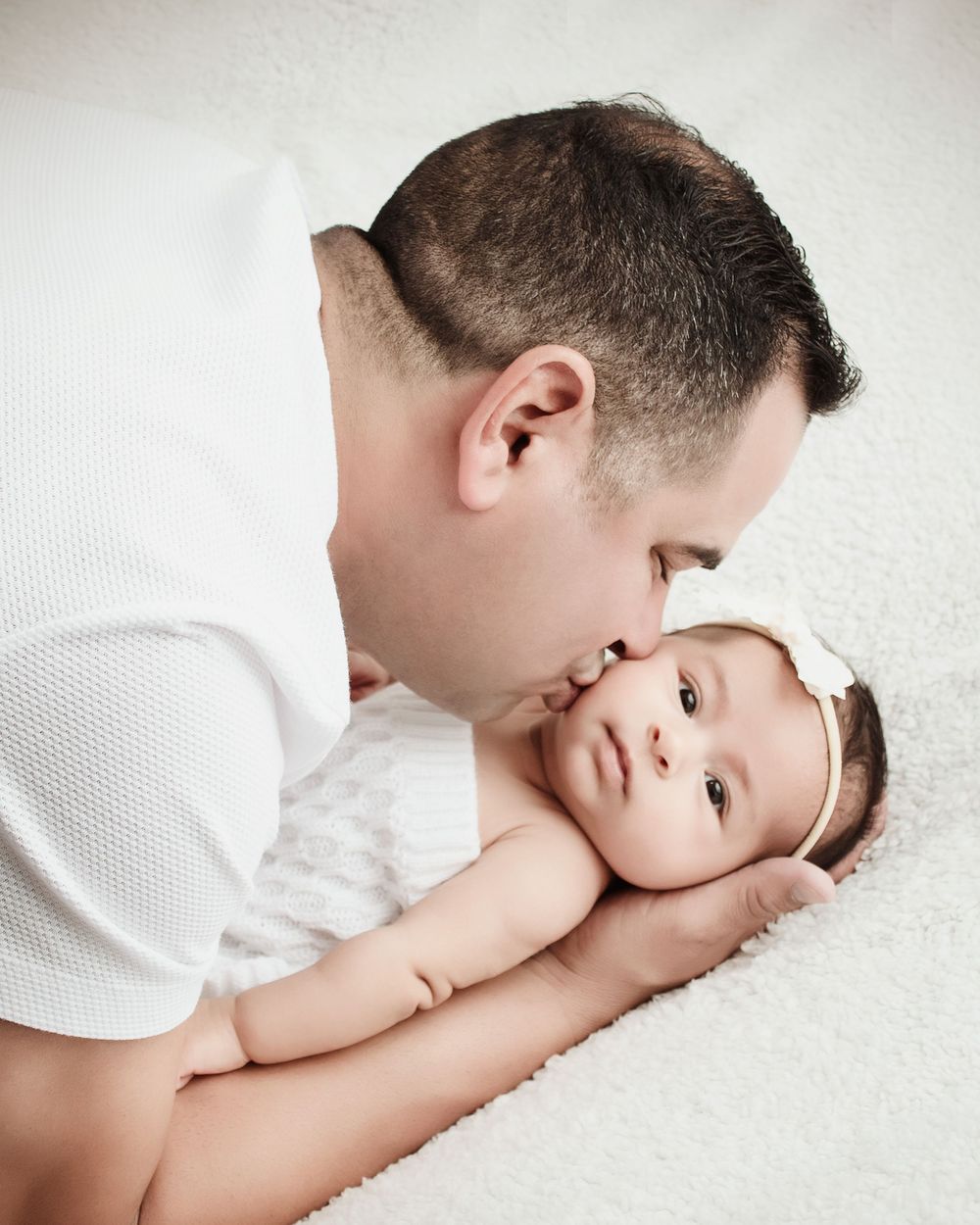 A sequence of touching moments between parent and small baby lying on soft white bedding.