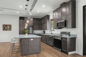 Modern kitchen with dark espresso cabinets, stainless steel appliances, a large quartz island with bar stools, pendant lights and hardwood f