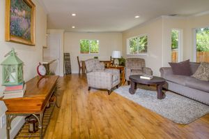Bright living room with hardwood floors, a gray sofa, cushioned armchairs, a wooden coffee table, an area rug and large windows.