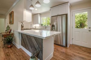 Bright modern kitchen with white cabinets, marble peninsula with reclaimed wood paneling, stainless steel refrigerator, and hardwood floors.