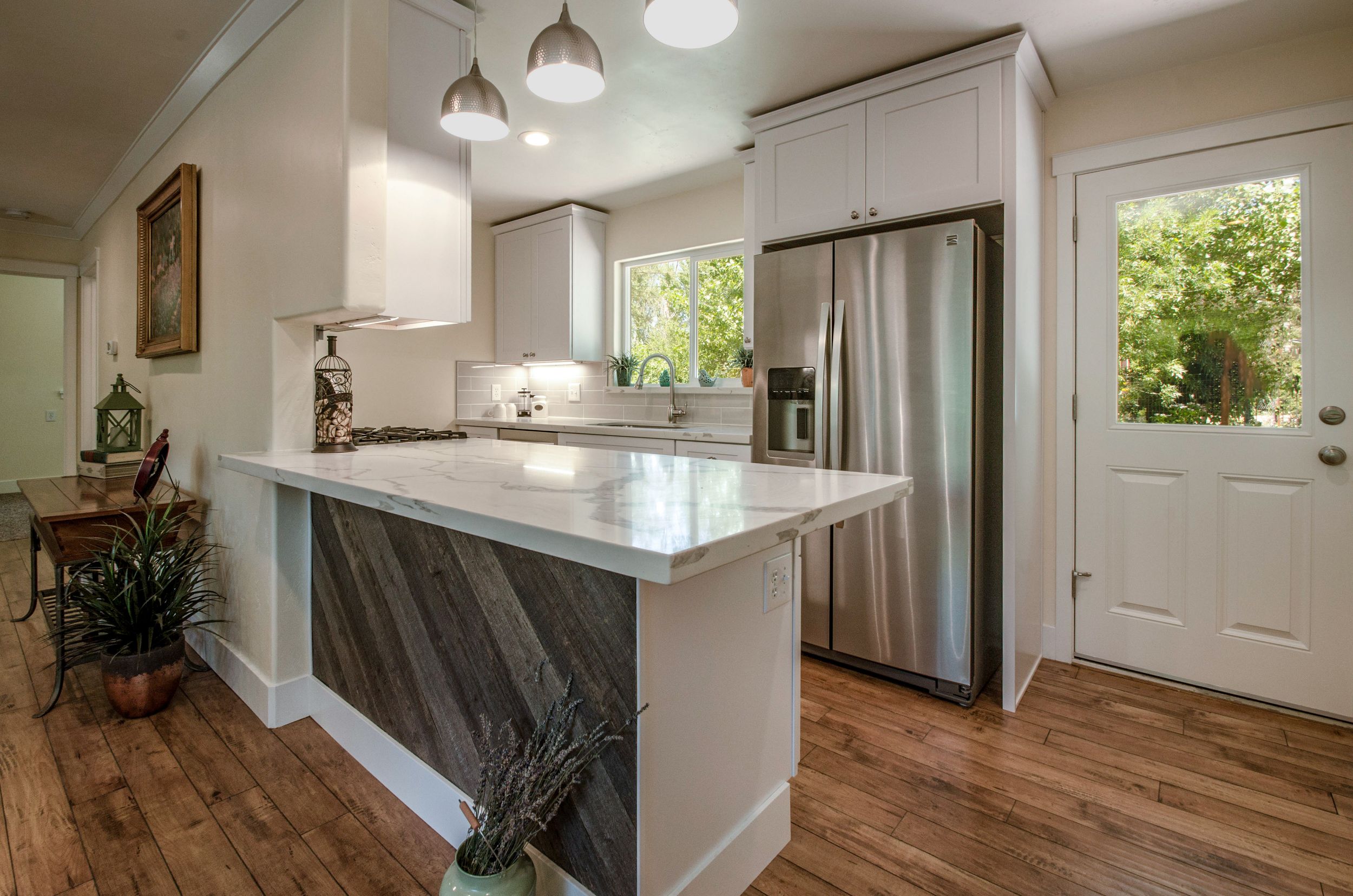 Modern kitchen with white cabinets, marble island, wood-panel base, stainless steel fridge, and hardwood floors.