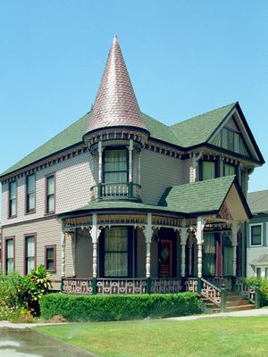 Victorian Queen Anne house with copper turret, wrap-around porch, ornate trim, and green roof in sunny California.