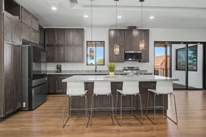 Modern kitchen with dark brown cabinets, a center island with white bar stools, pendant lights, stainless appliances, and hardwood floors.