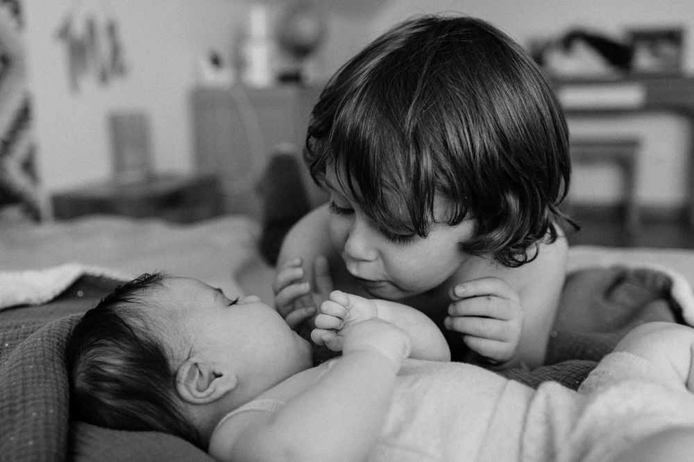 Moment tendre et complice entre un grand frere et sa petite soeur capture par une photographe famille Lille lors d'une seance a domicile
