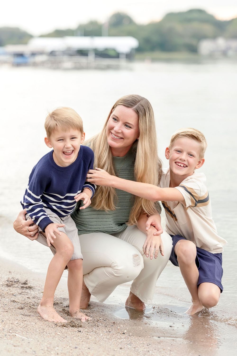 A joyful family moment at the beach as they laugh and play together in the sand near the water's edge.