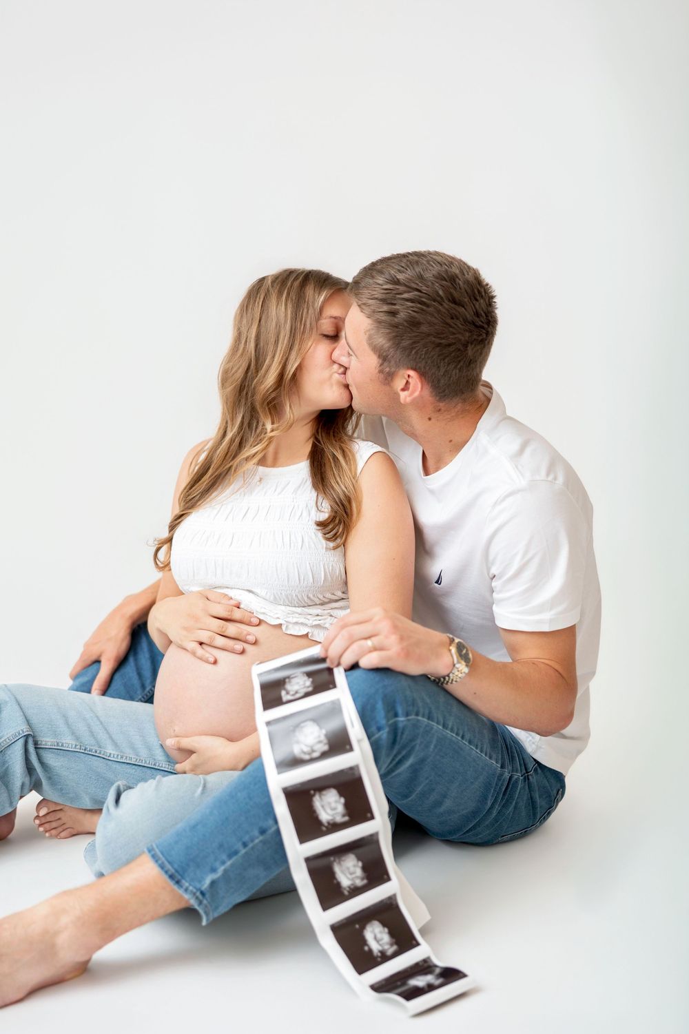 Pregnancy announcement in white tops and jeans with ultrasound photos during a timeless studio session in Clear Lake, Iowa