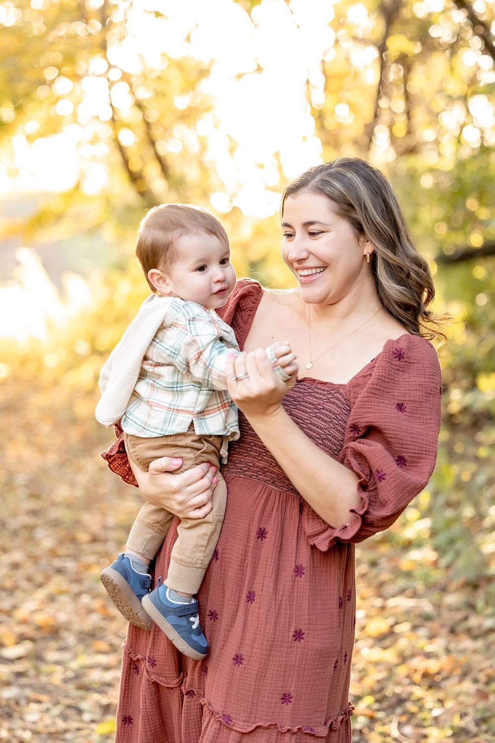 A parent and baby share joyful moments together on an autumn day surrounded by golden fallen leaves.