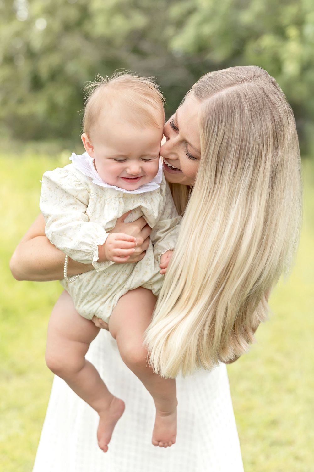 Joyful outdoor portrait showing affectionate moment between parent and baby in white outfits.