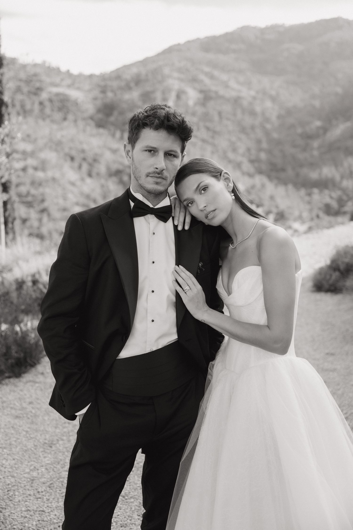 A couple in wedding attire crossing a cobblestone street in an elegant European city setting.