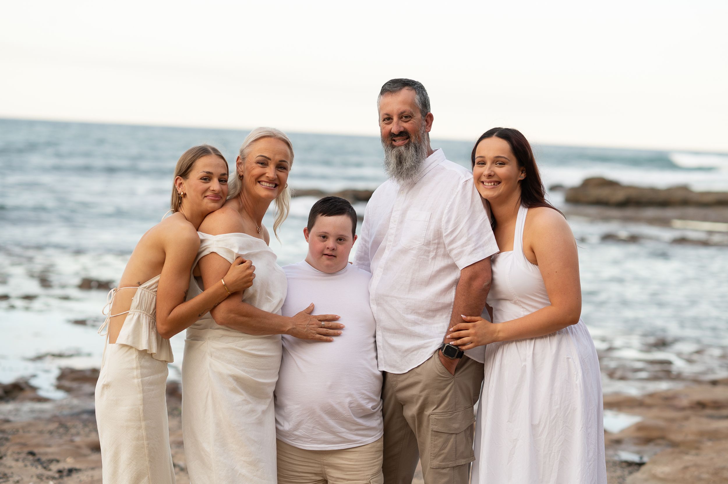 A happy group stands together on a rocky beach at sunset with ocean waves in the background.
