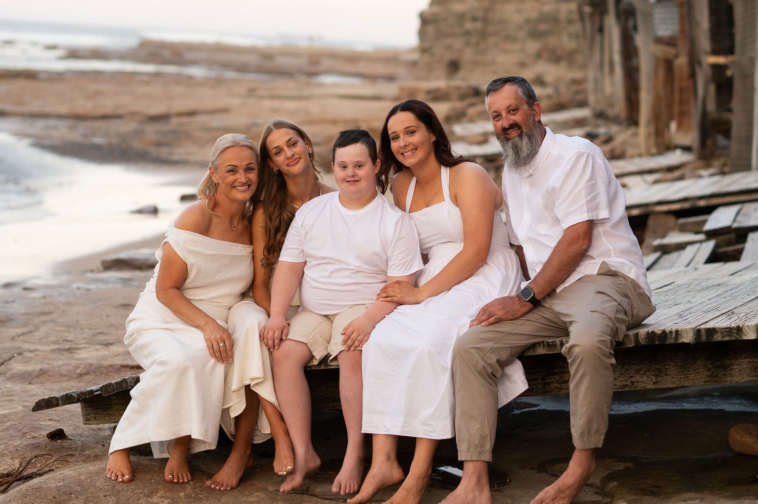 A group of people sitting together on wooden steps at the beach during golden hour.
