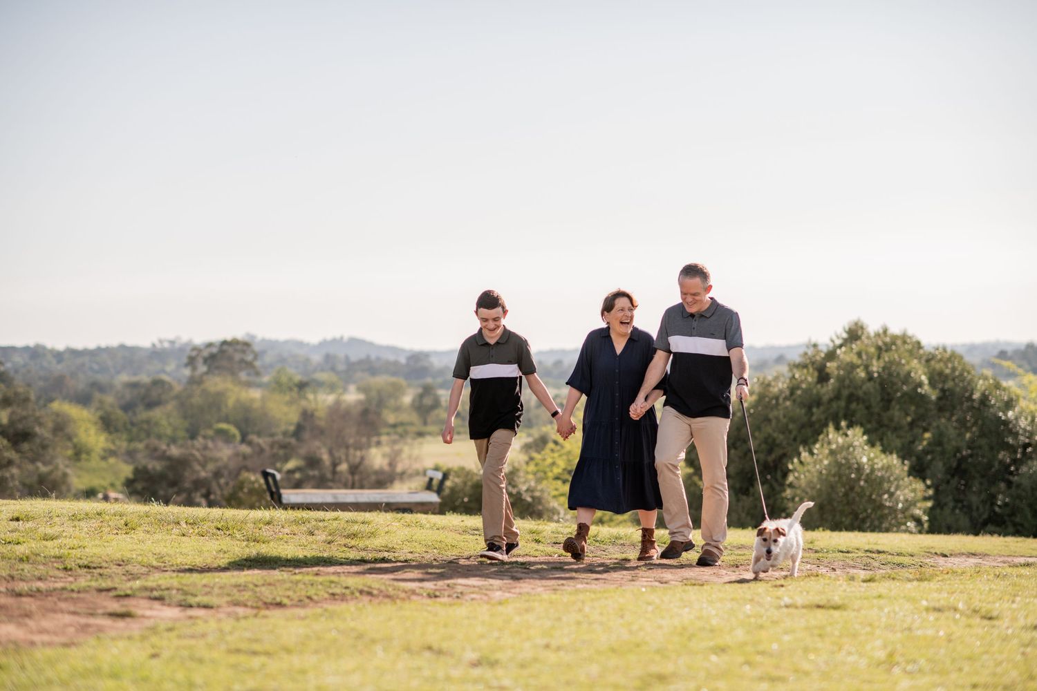 A small group takes an evening stroll with their dog on a grassy hilltop overlooking scenic countryside landscape.