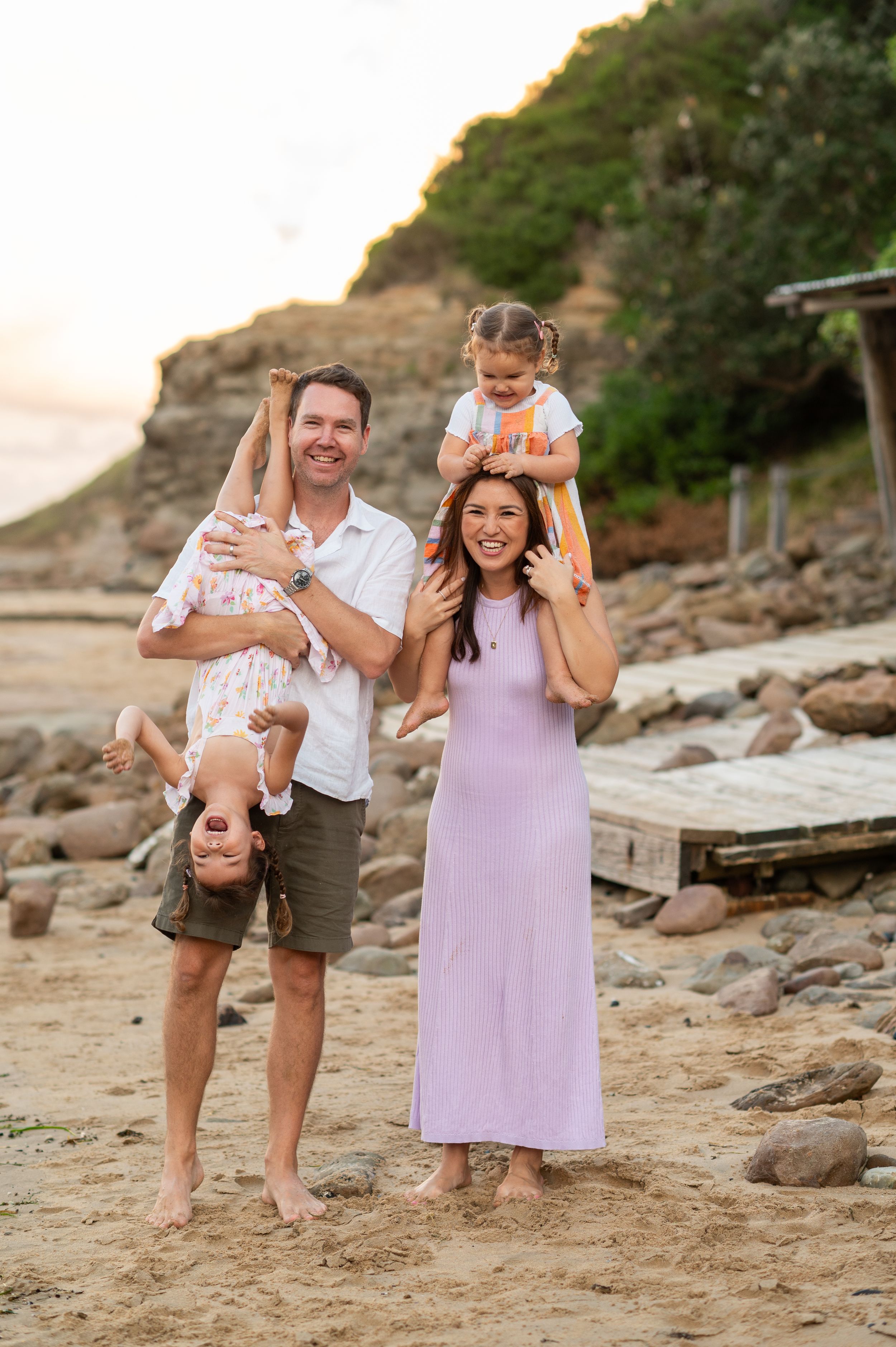 Family enjoying sunset together on rocky beach with cliffs in background.