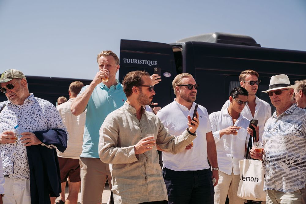 A group of people gathered outdoors on a sunny day, holding drinks and engaged in conversation.