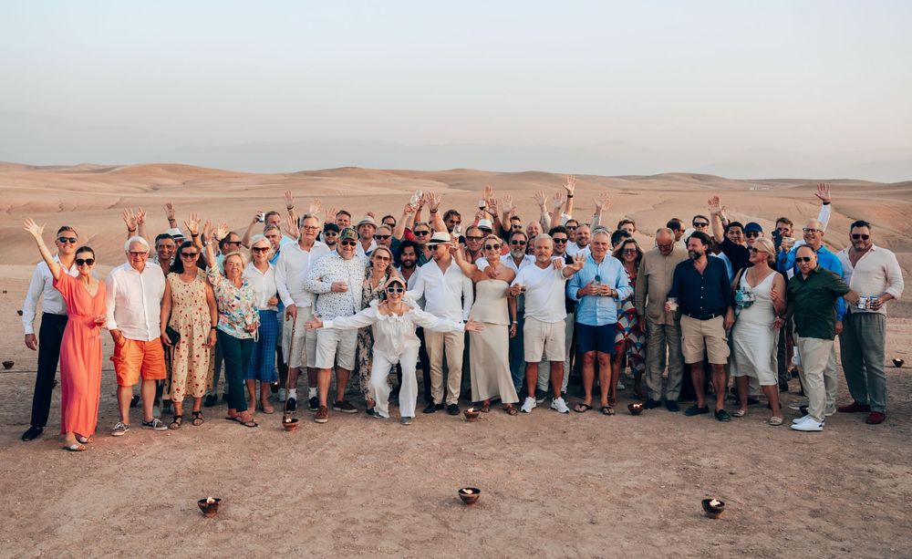 A large group poses together in casual attire against a desert landscape backdrop during daytime.