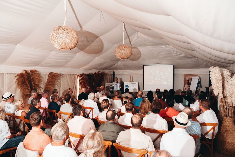 Large wedding reception tent filled with guests seated at round tables with soft paper lantern lighting overhead.