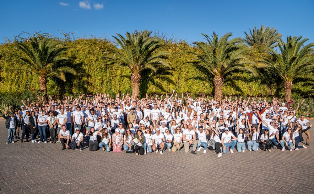 A panoramic view of a large crowd gathered outdoors with palm trees and blue sky in the background.