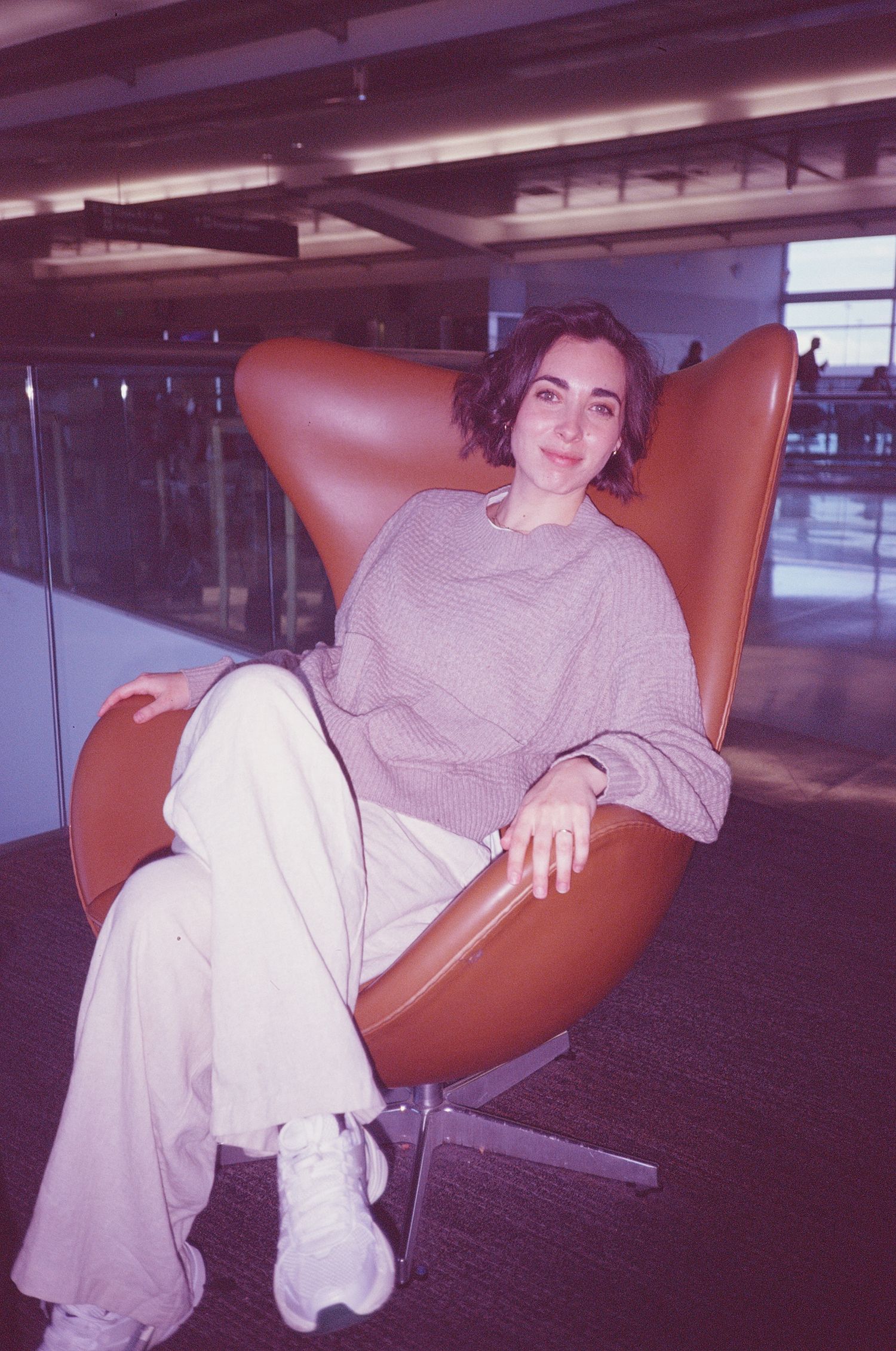 Person relaxing in retro brown leather chair in modern office space.
