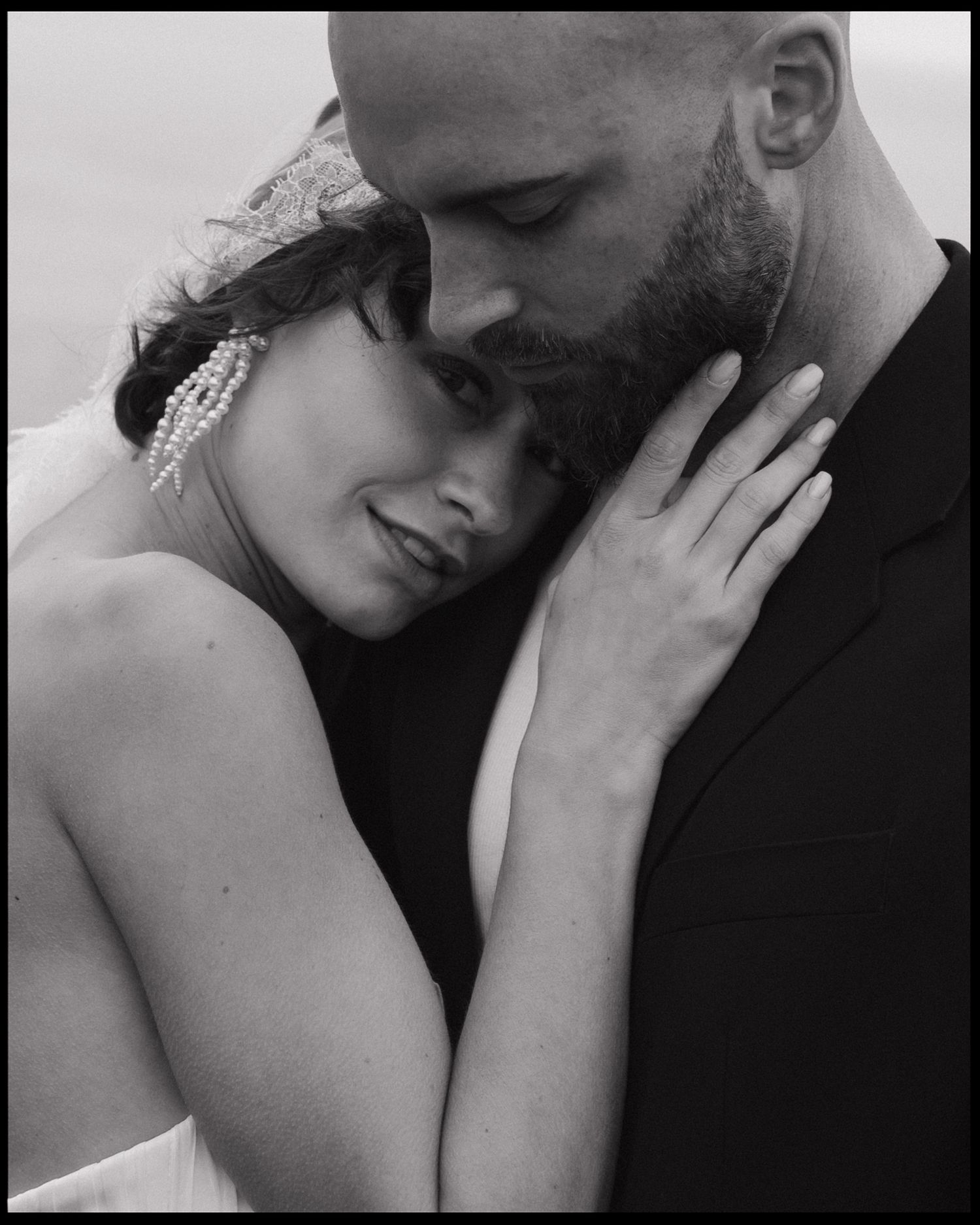 A candid black and white photo of a bride laughing in a field with her groom.