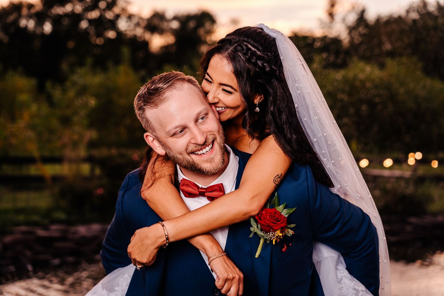 Candid moment of newlyweds laughing and embracing during sunset wedding photos by the water.