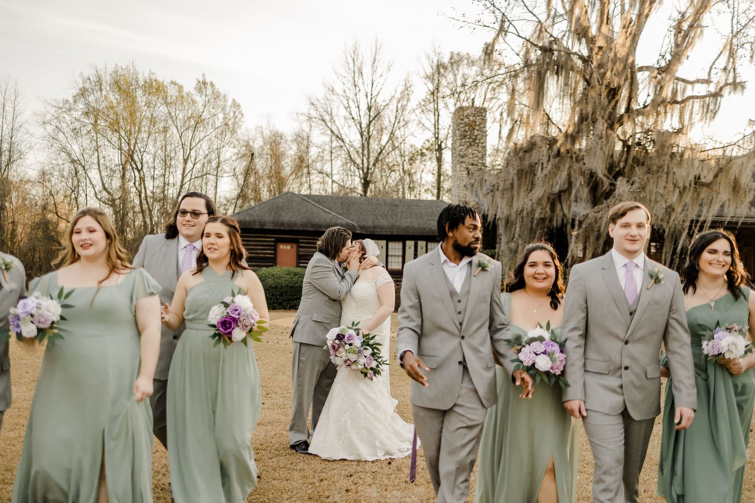 Wedding party in sage green and gray attire poses together outdoors.