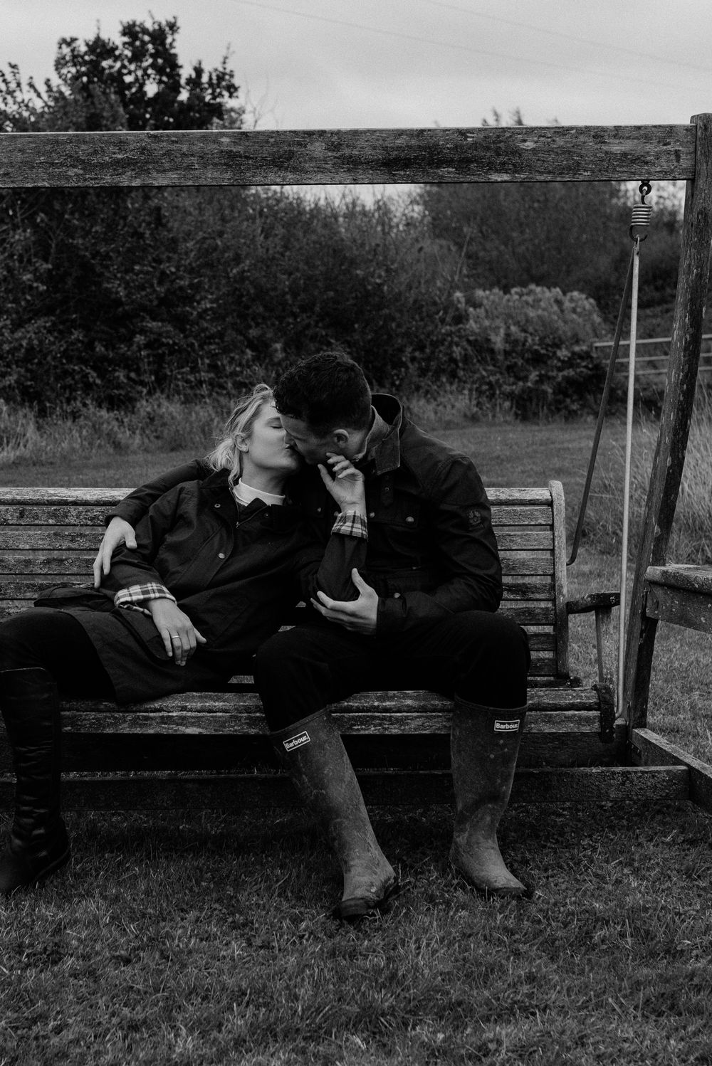 Vintage black and white photo of couple relaxing on wooden bench in rural setting.