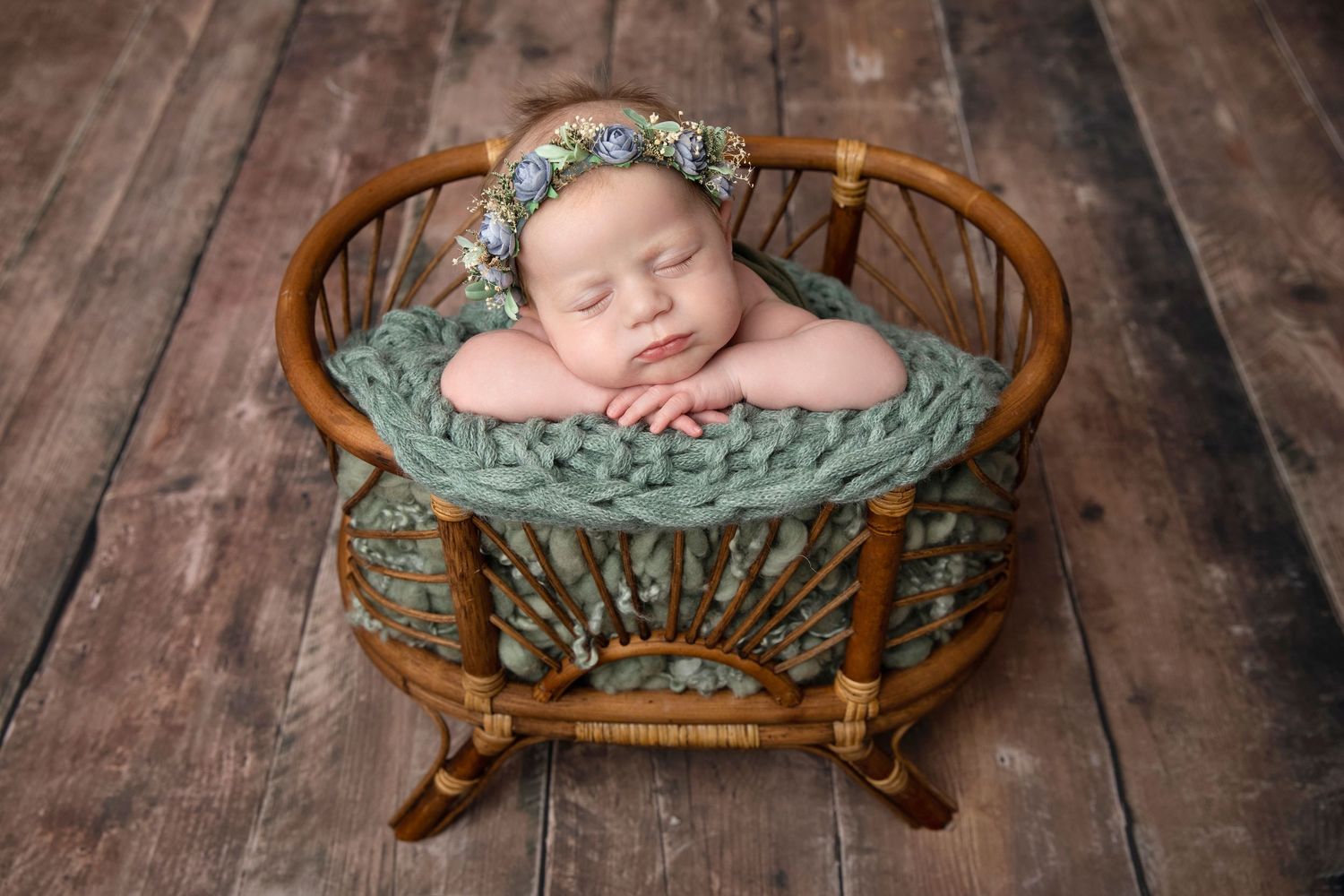 Peaceful newborn sleeping in round basket with green blanket on wooden floor.