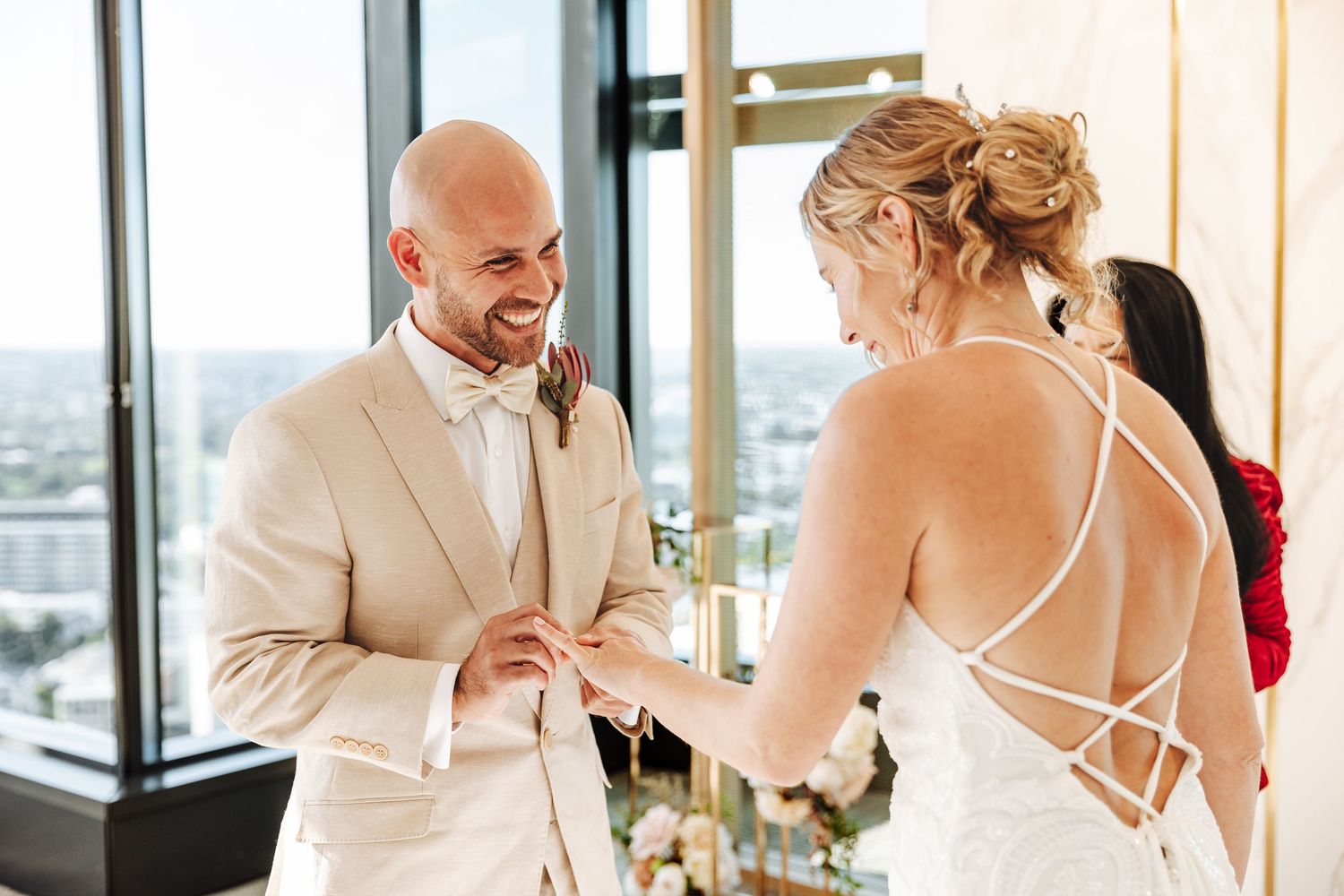 A bride and groom share a joyful moment during their wedding ceremony at Brisbane Registry in a bright room with city views.