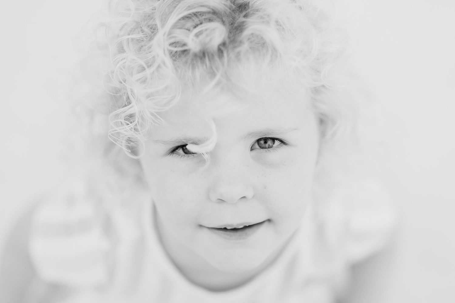 Close-up black and white portrait of a child with curly hair and bright eyes.