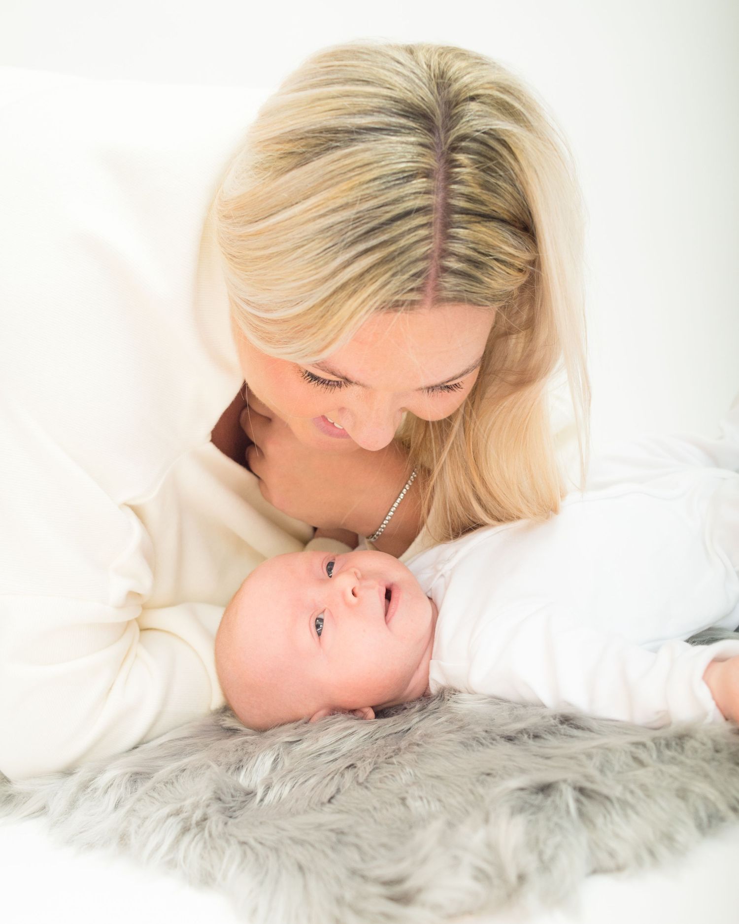 A woman rests on a fur blanket smiling at her new baby, showcased in newborn photography by Abigail's Studio located in Buckinghamshire.