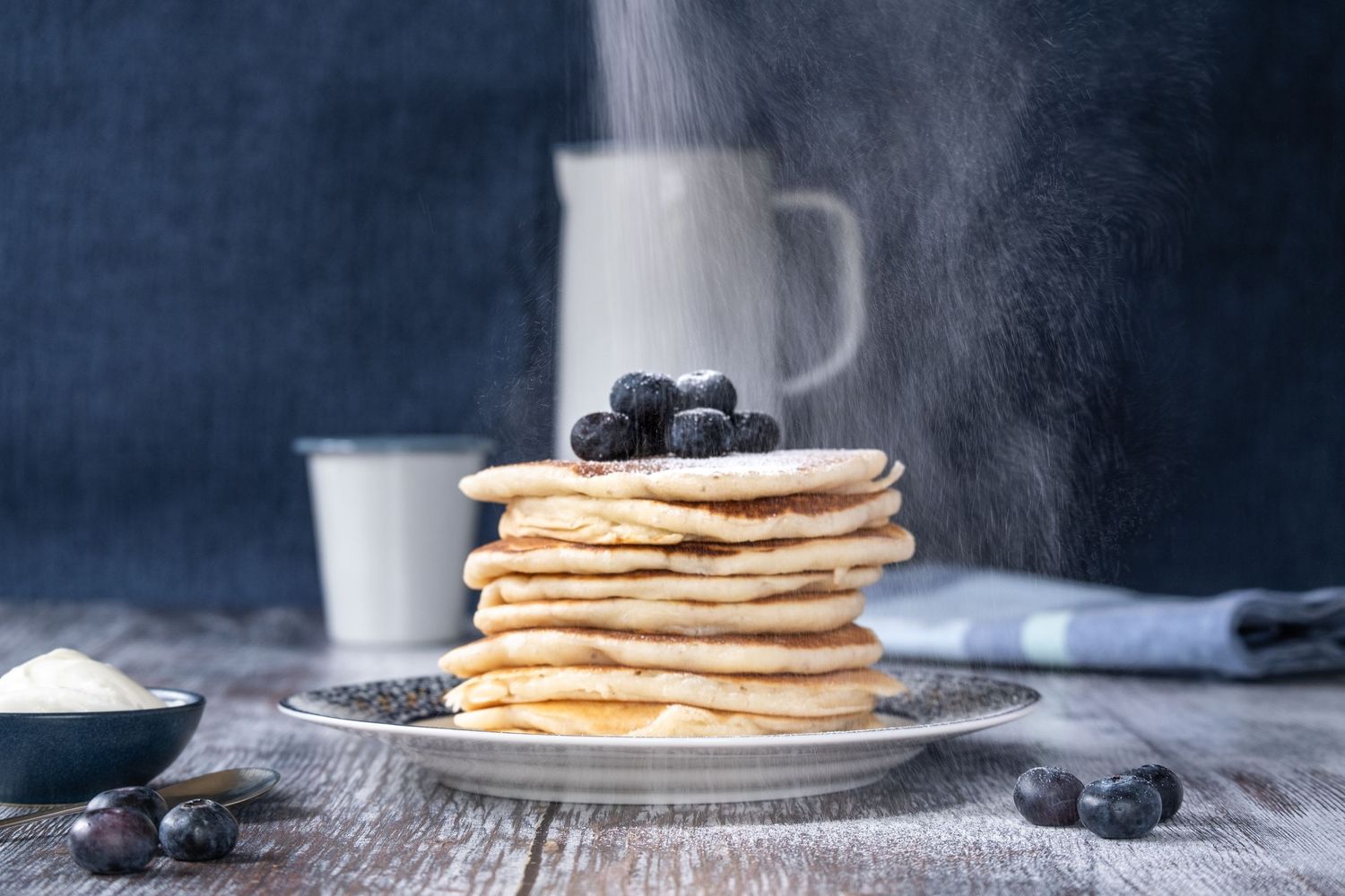 stack of home baked pancakes with icing sugar falling