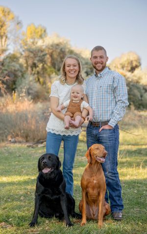 Happy family portrait outdoors with their two dogs, a black lab and vizsla.