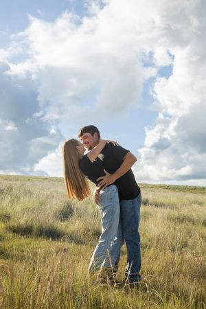 A couple embraces romantically in a sunlit meadow of tall grass during a golden hour photo session.