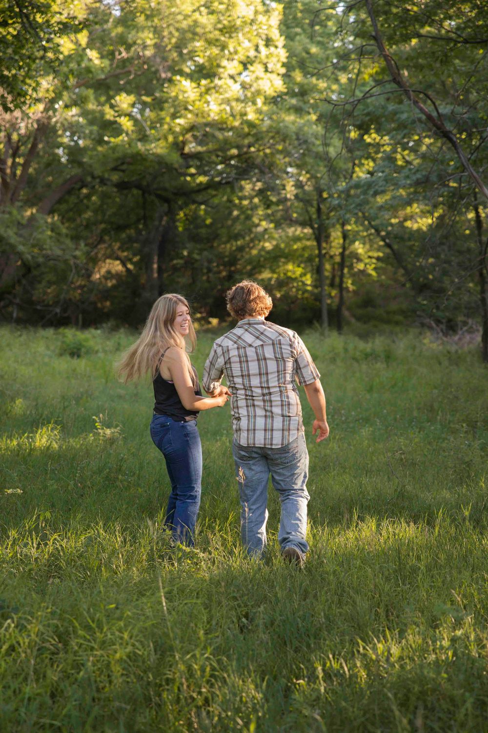 A couple walks together through a sunlit meadow on a warm summer evening.
