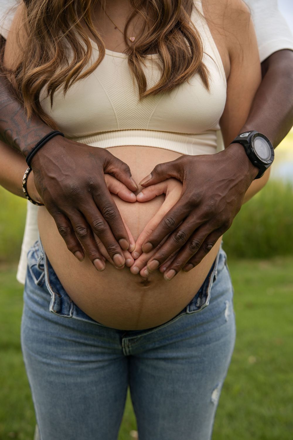 Closeup progression of dark hands holding a pregnant belly wearing a cream top and blue jeans against an outdoor background.
